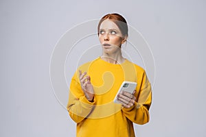 Uptight young woman holding mobile phone and looking at camera on isolated white background.