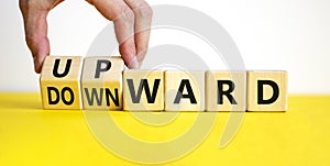 Upward or downward symbol. Businessman turns wooden cubes and changes the word `downward` to `upward`. Beautiful yellow table,