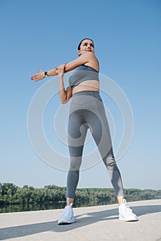 Upward photo of a confident young woman doing her stretches. Over blue sky