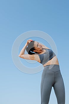 Upward photo of a young woman in sportswear doing her stretches. Over blue sky
