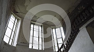 Upward view of abandoned old mansion with wooden staircase and large windows.