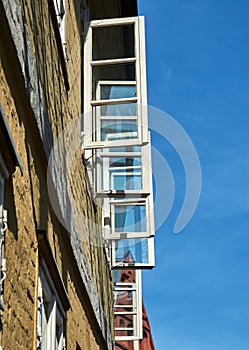 Upward view along a house wall with open windows with white painted window frames in front of a blue sky