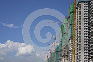 Upward view of precast building cover by green net, large tall Tower Crane moving machine in construction work, under clear blue