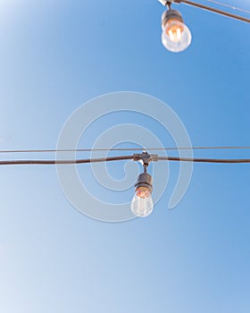 Upward view string wired Illuminated bulbs on clear blue sky background