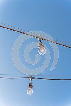 Upward view string wired Illuminated bulbs on clear blue sky background