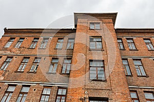 Upward view to old red brick wall building with windows and cloudy sky on the background