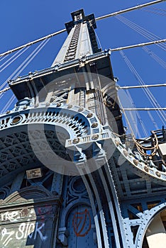 Upward view of a tower of the Manhattan Bridge with curved decorative steel work painted blue
