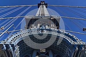 Upward view of a tower of the Manhattan Bridge with curved decorative steel work painted blue