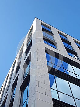 Upwards view of the corner of a white modern office building with blue sky and clouds reflected in large glass windows