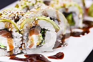 Uramaki sushi roll with smoked eel and unagi on white plate over black background. Japanese cuisine concept