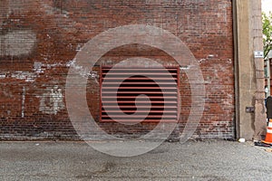 Urban alley alongside an old red brick industrial building with a large commercial HVAC exhaust vent, industrial background