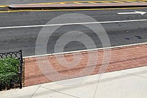 Urban asphalt street with traffic island, curb with red brick border and concrete sidewalk, city street creative copy space