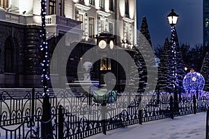 Urban background night christmas landscape, city clock and lights with garlands on the square