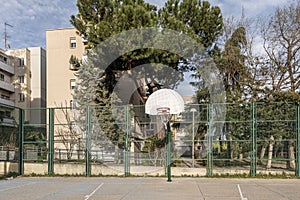 An urban basketball court with rough cement floors, a perimeter with metal fences and baskets on metal posts screwed to the ground