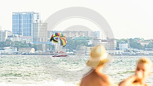 Urban beach with cityscape, sunbathers and parasailing boat