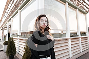 Urban beautiful young woman in a black coat in a fashionable t-shirt in white jeans with a pose posing