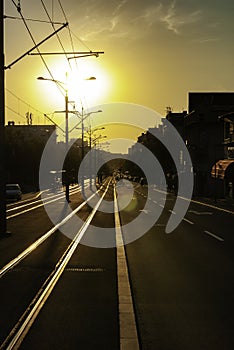 Urban city sunset vertical image of city street boulevard direct sunlight lens flare tram track tramway rails empty street