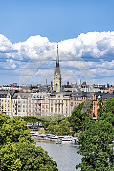 Urban cityscape featuring a clock tower and trees in the foreground: Stockholm city