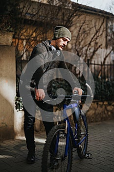 Urban cyclist with headphones resting by his bike on a city street