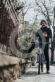 Urban cyclist taking a break to check his smart phone on city sidewalk