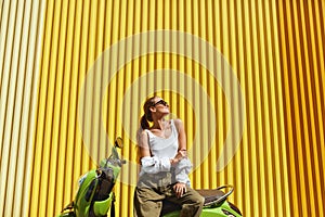 Urban. Fashion Girl On Moped Portrait. Sexy Model In Casual Clothes And Sunglasses Against Yellow Metal Fence