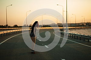 Urban fashionable girl riding longboard outdoors on the road at sunset.