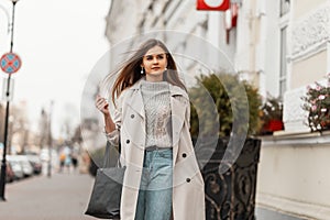 Urban fashionable young woman walks outdoors in the city. Modern brown-haired girl model in stylish outerwear with a trendy