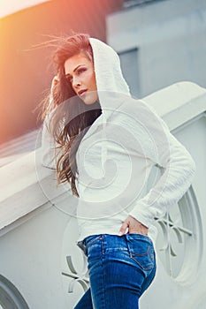 Urban girl  in blue jeans and white sweater  with hood  summer day in city