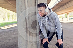 Urban handsome man runner with earphones taking break