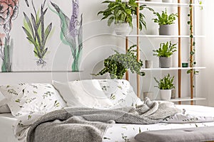 Urban jungle bedroom interior with plants in pots beside a bed dressed in organic cotton linen of white color with green print. Re