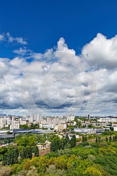 An urban landscape with a green park, residential areas and a TV tower against a bright blue sky with thickening clouds