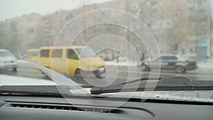 Urban landscape silhouettes of driving cars and tram from windshield of car with wipers in winter