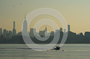 Urban landscape of skyscrapers of Manhattan, New York, with cutter running and birds flying low above the water ahead