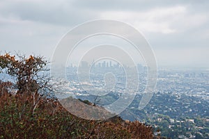 Urban landscape view of Los Angeles skyline under cloudy sky, with hillsides and residential areas.