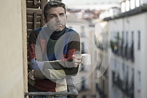 Urban lifestyle emotional portrait of young attractive man sad and depressed at home balcony drinking coffee cup suffering