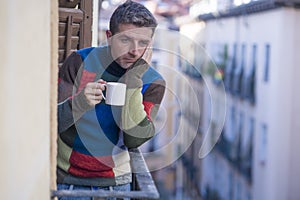 Urban lifestyle emotional portrait of young attractive man sad and depressed at home balcony drinking coffee cup suffering