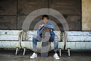 Urban lifestyle portrait of young handsome and attractive black afro American skateboarder man sitting on city grunge bench