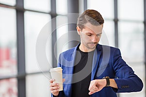 Urban man with coffee inside in airport. Casual young boy wearing suit jacket. Caucasian man with cellphone at the