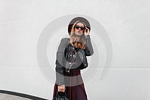 Urban modern young woman hipster in fashionable clothes with a leather backpack in a purple hat posing standing