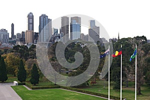Urban park with trees, grass, flagpoles and iconic cityscape of modern skyscrapers in Melbourne downtown, Victoria, Australia