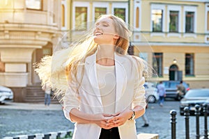 Urban portrait of beautiful young blonde woman with long hair flying in wind