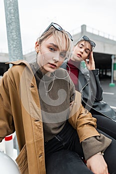 Urban portrait of beautiful young women with leather jacket and sweater in black jeans sits and poses on the street