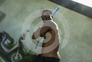 Urban portrait of young aggressive and upset violent black African American man using baseball bat threatening at grunge corner in