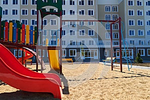 Urban residential infrastructure without people - children`s playground next to a condominium. Swing, slide, stairs, multistory