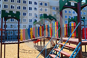 Urban residential infrastructure without people - children`s playground next to a condominium. Swing, slide, stairs, multistory