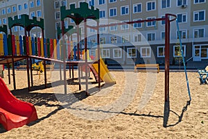 Urban residential infrastructure without people - children`s playground next to a condominium. Swing, slide, stairs, multistory