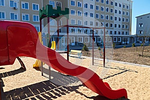 Urban residential infrastructure without people - children`s playground next to a condominium. Swing, slide, stairs, multistory