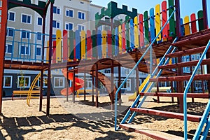 Urban residential infrastructure without people - children`s playground next to a condominium. Swing, slide, stairs, multistory