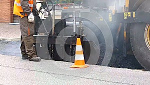 Urban road under construction, asphalting in progress. Worker in orange uniform.