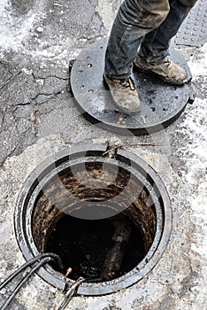 Urban road under construction, asphalting in progress, workers near sewer manhole, feet fragment